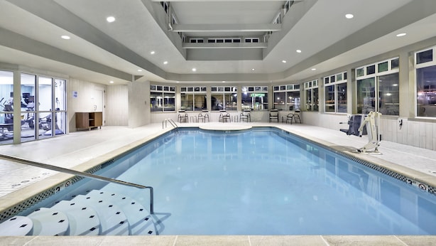 Uma grande piscina interior com água cristalina, rodeada por áreas de estar e vista para a cidade através de amplas janelas.