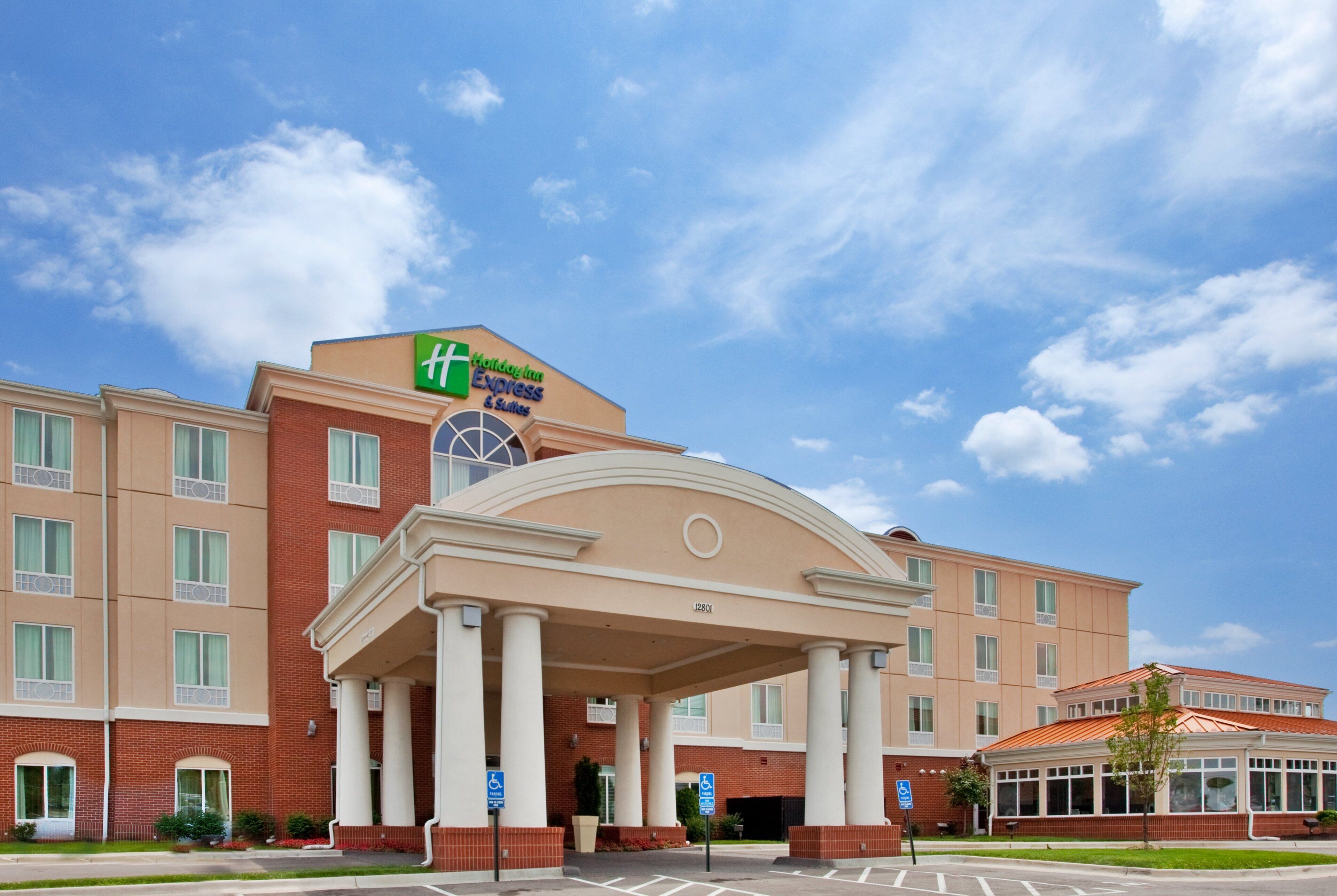 A Holiday Inn Express & Suites hotel with a prominent entrance, multiple windows, and a clear sky.
