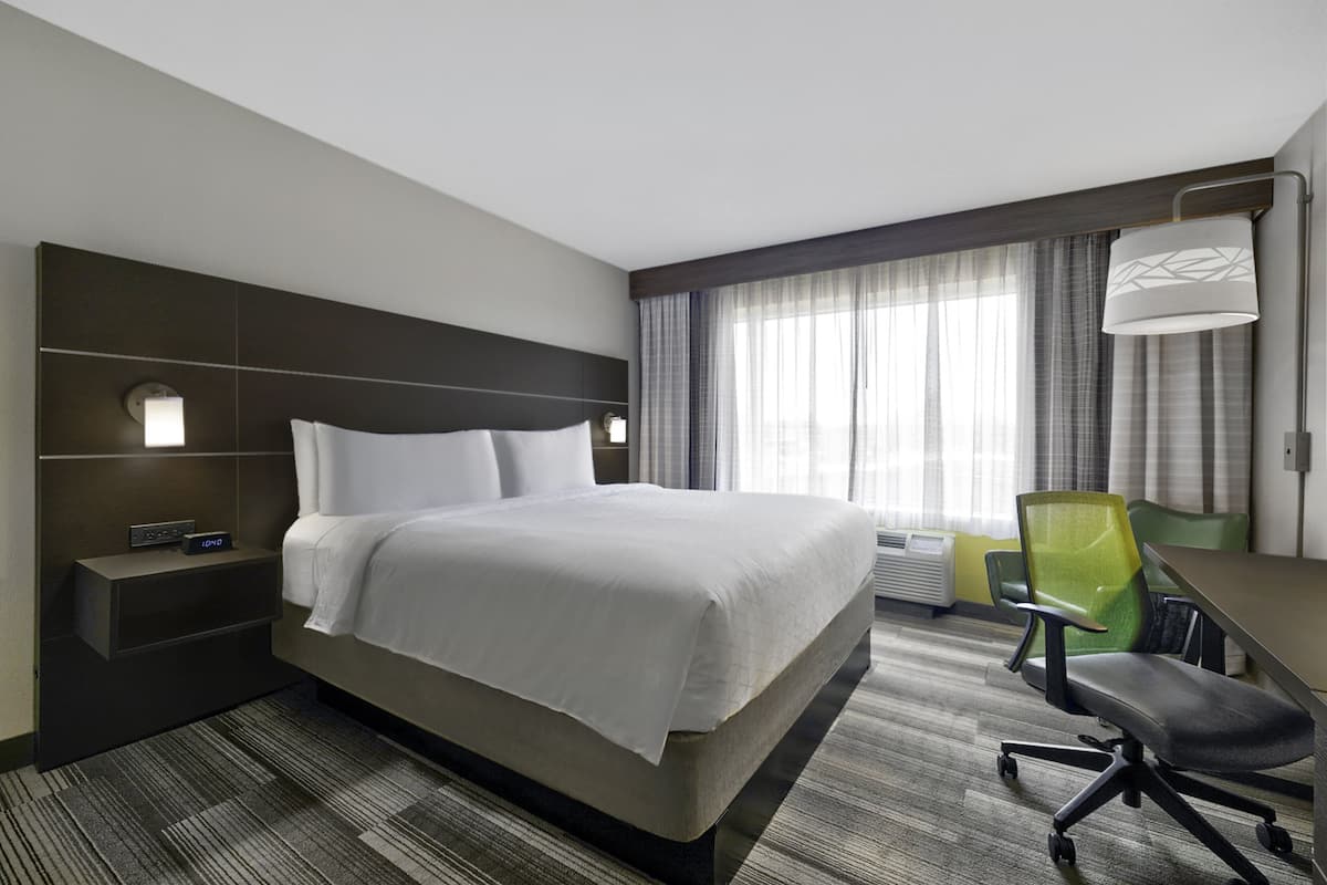 Une chambre d’hôtel avec un grand lit, un bureau avec une chaise, une table de chevet et une fenêtre avec des rideaux.