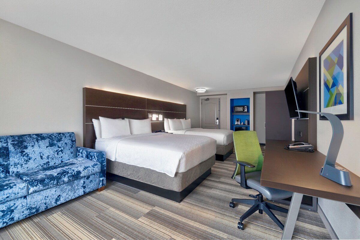 A hotel room with a bed, a sofa, a desk, and a television.