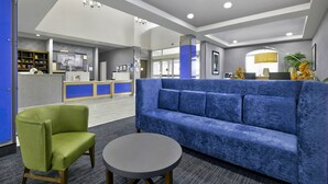 Um hall moderno com um sofá azul, uma poltrona verde e uma mesa redonda.