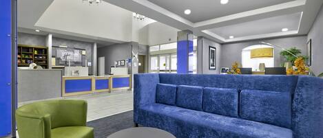 A modern lobby with a blue sofa, green armchair, and a round table.