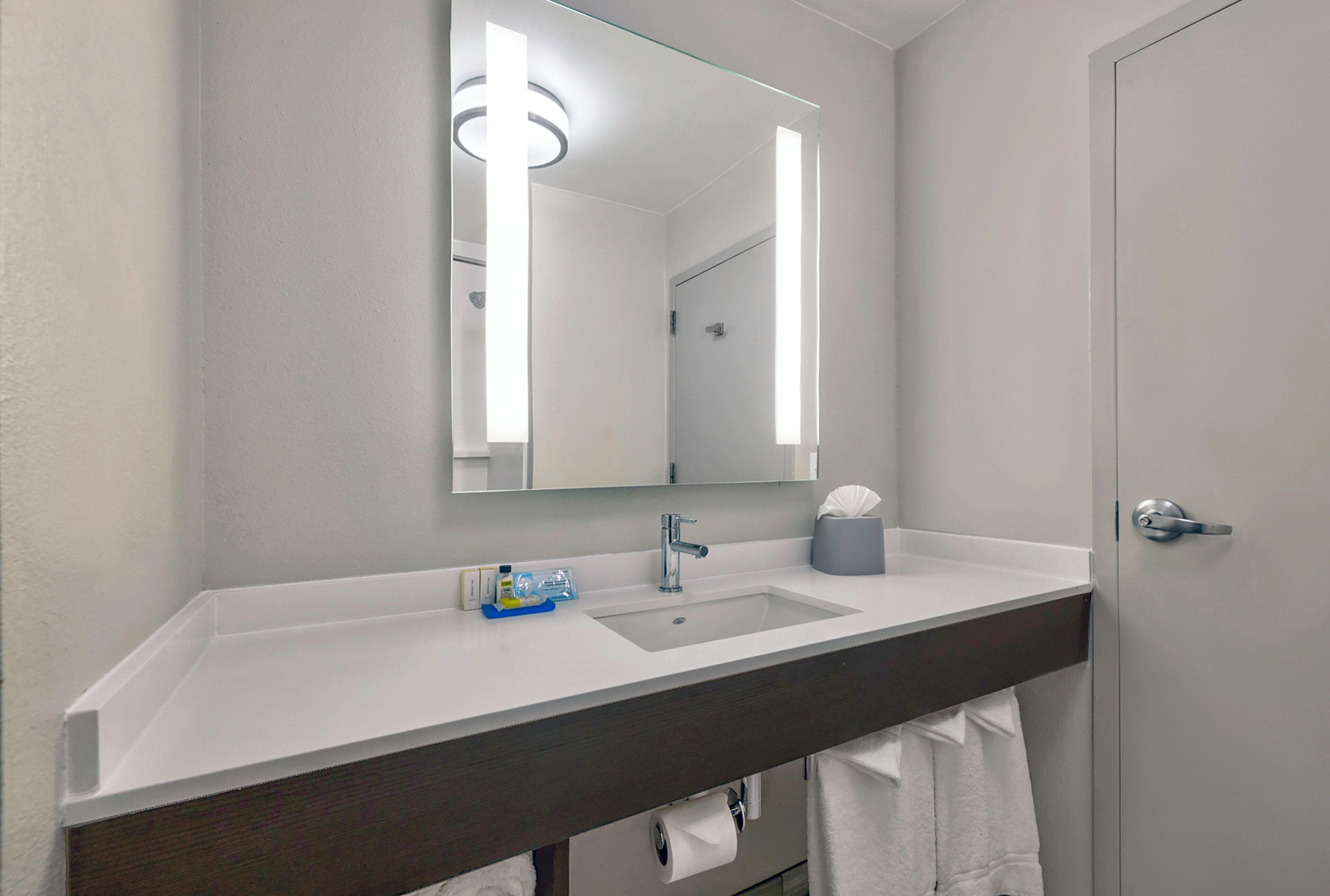 Un baño con lavamanos blanco, espejo y barra para toallas.
