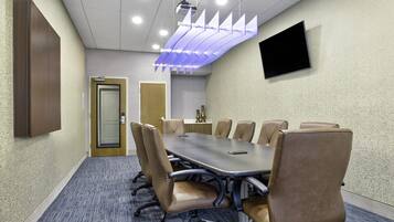 A conference room with a long table, several chairs, a flat-screen TV, and a ceiling projector.