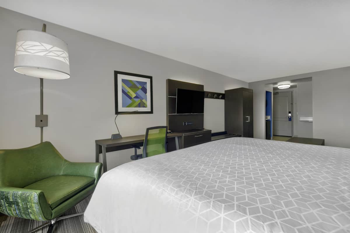 Une chambre d’hôtel avec un grand lit, un bureau avec une chaise, une télévision et une lampe.