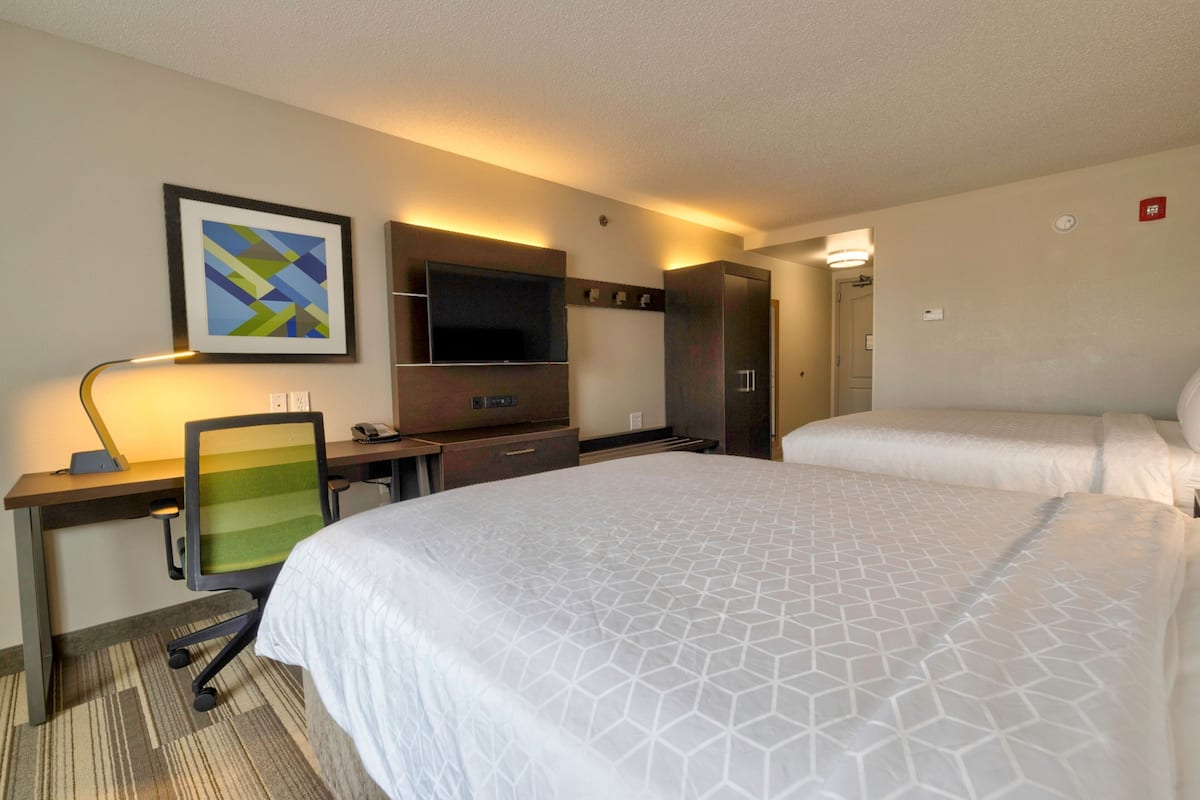 Une chambre d’hôtel avec deux lits, un bureau avec une chaise, un téléviseur à écran plat et un tableau encadré au mur.