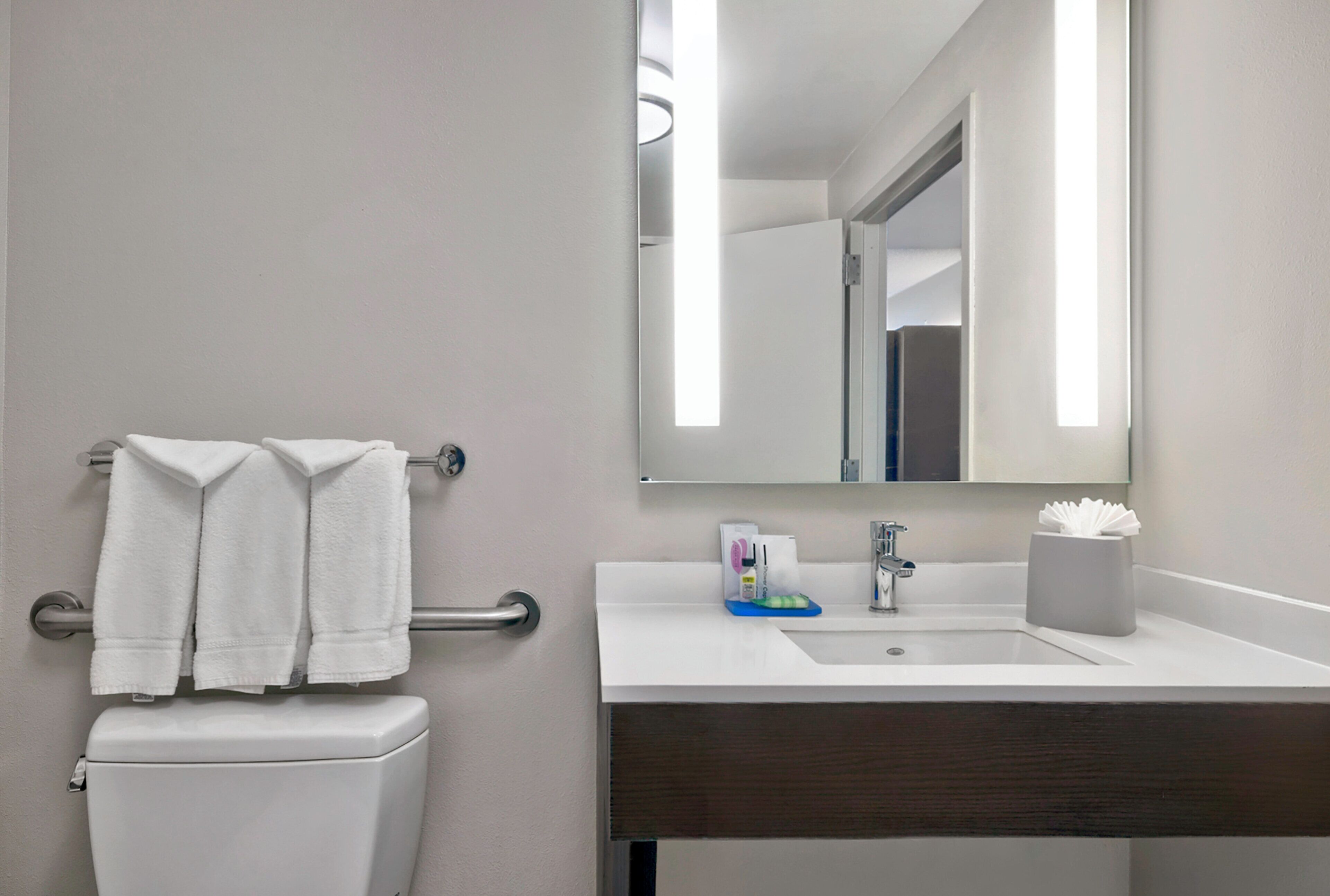 A modern bathroom with a toilet, a sink, a mirror, and a towel rack.