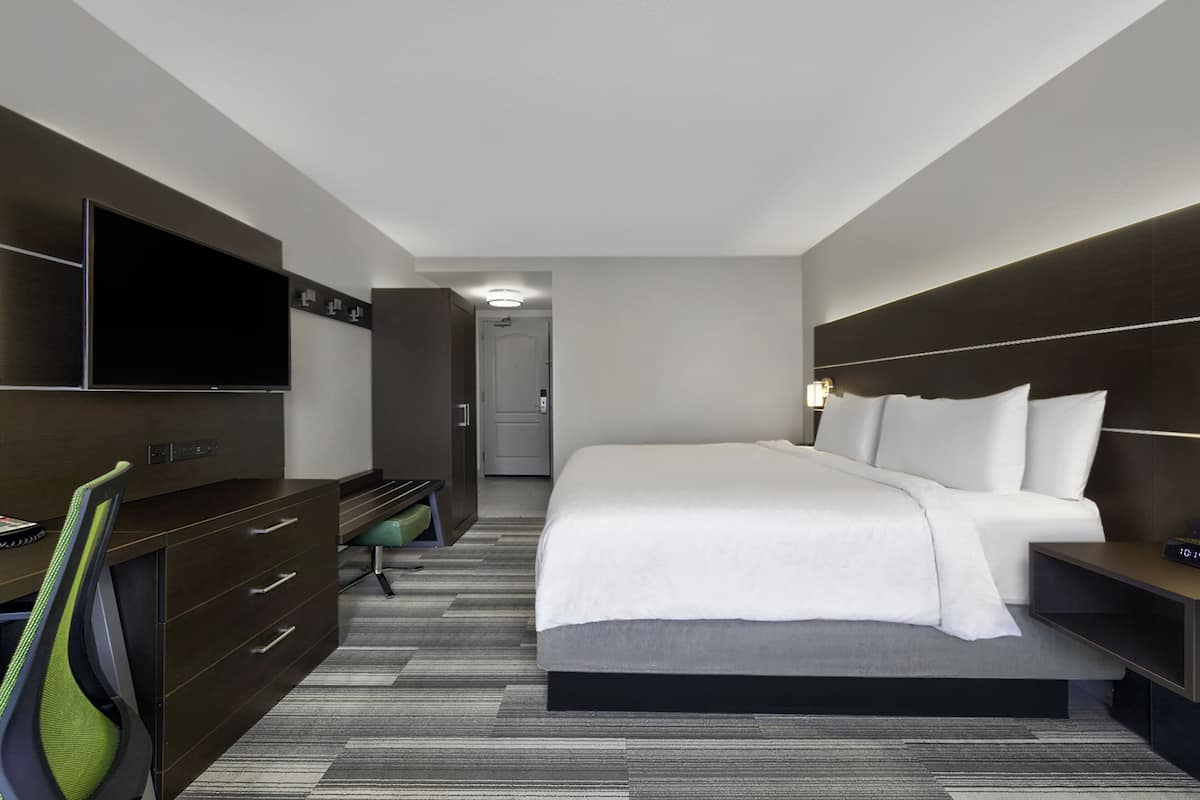 Une chambre d’hôtel moderne dotée d’un grand lit, d’une télévision à écran plat, d’un bureau avec une chaise et d’un dressing.