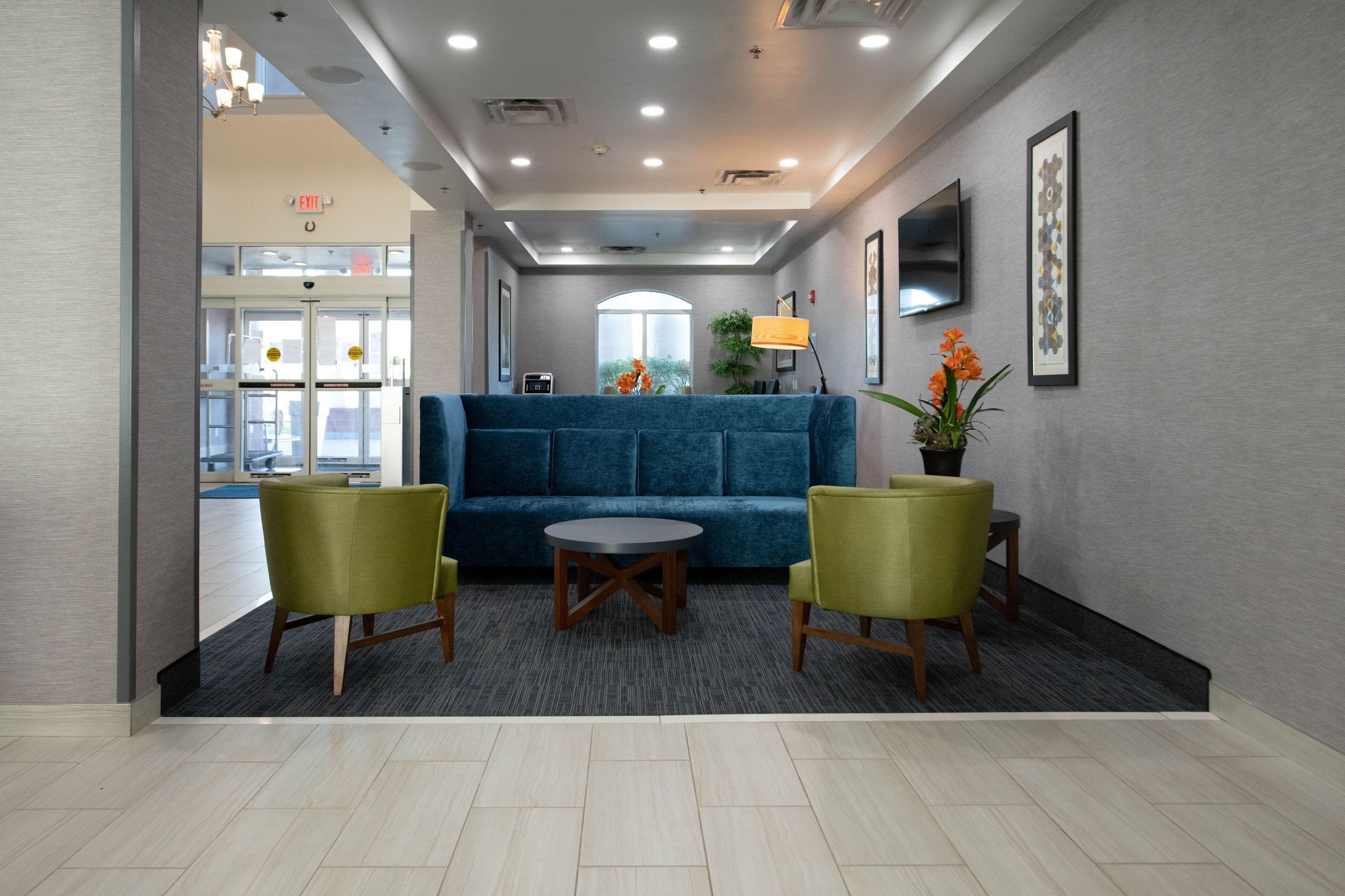 Eine Lobby mit einem blauen Sofa, zwei grünen Sesseln, einem kleinen runden Tisch und einem Topfpflanzen.