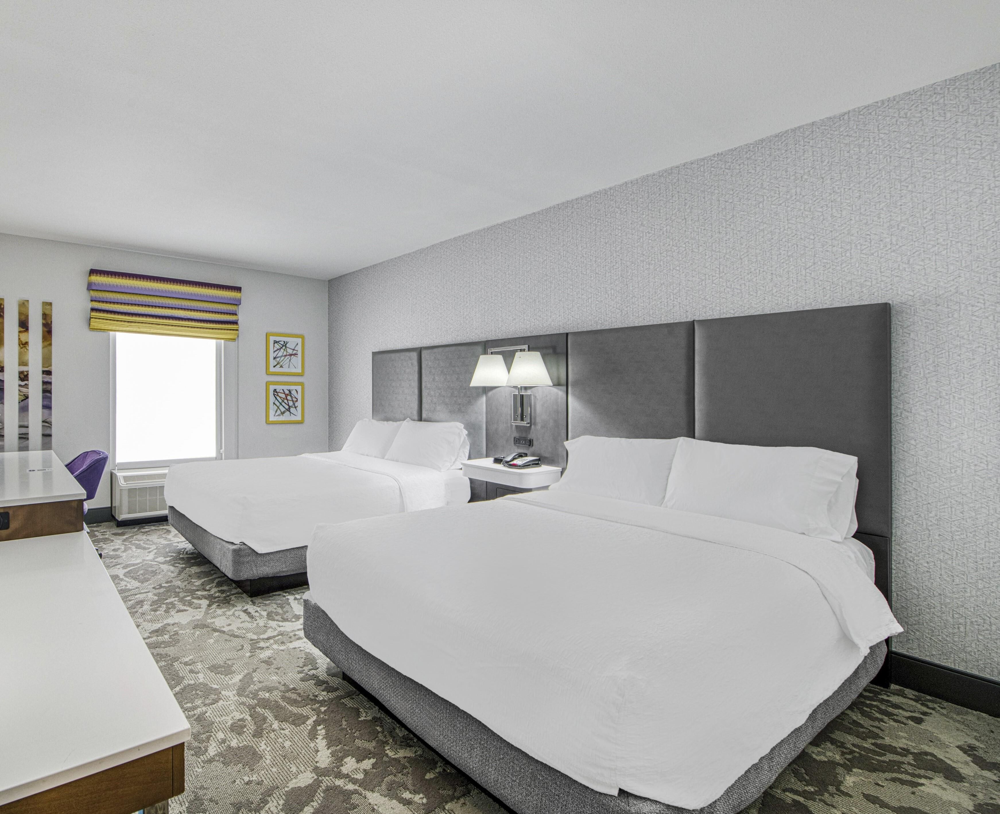 A hotel room with two beds, a desk, a chair, and a window with a view.