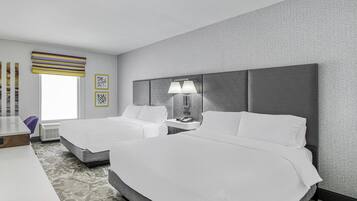 A hotel room with two beds, a desk, a chair, and a window with a view.
