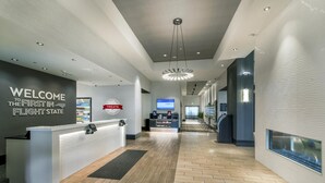 A reception area with a counter, a welcome sign, a digital screen, and a hallway leading to a dining area. - Hampton Inn & Suites Raleigh-Durham Airport-Brier Creek (Raleigh)