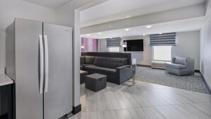 A modern kitchen with a built-in refrigerator, a gray sofa, and a gray armchair. - Hampton Inn & Suites Raleigh-Durham Airport-Brier Creek (Raleigh)