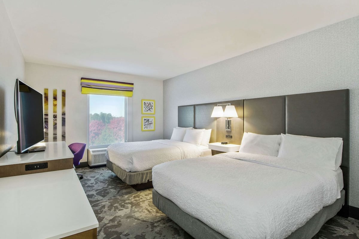 A hotel room with two beds, a desk, a television, and a window with a view.
