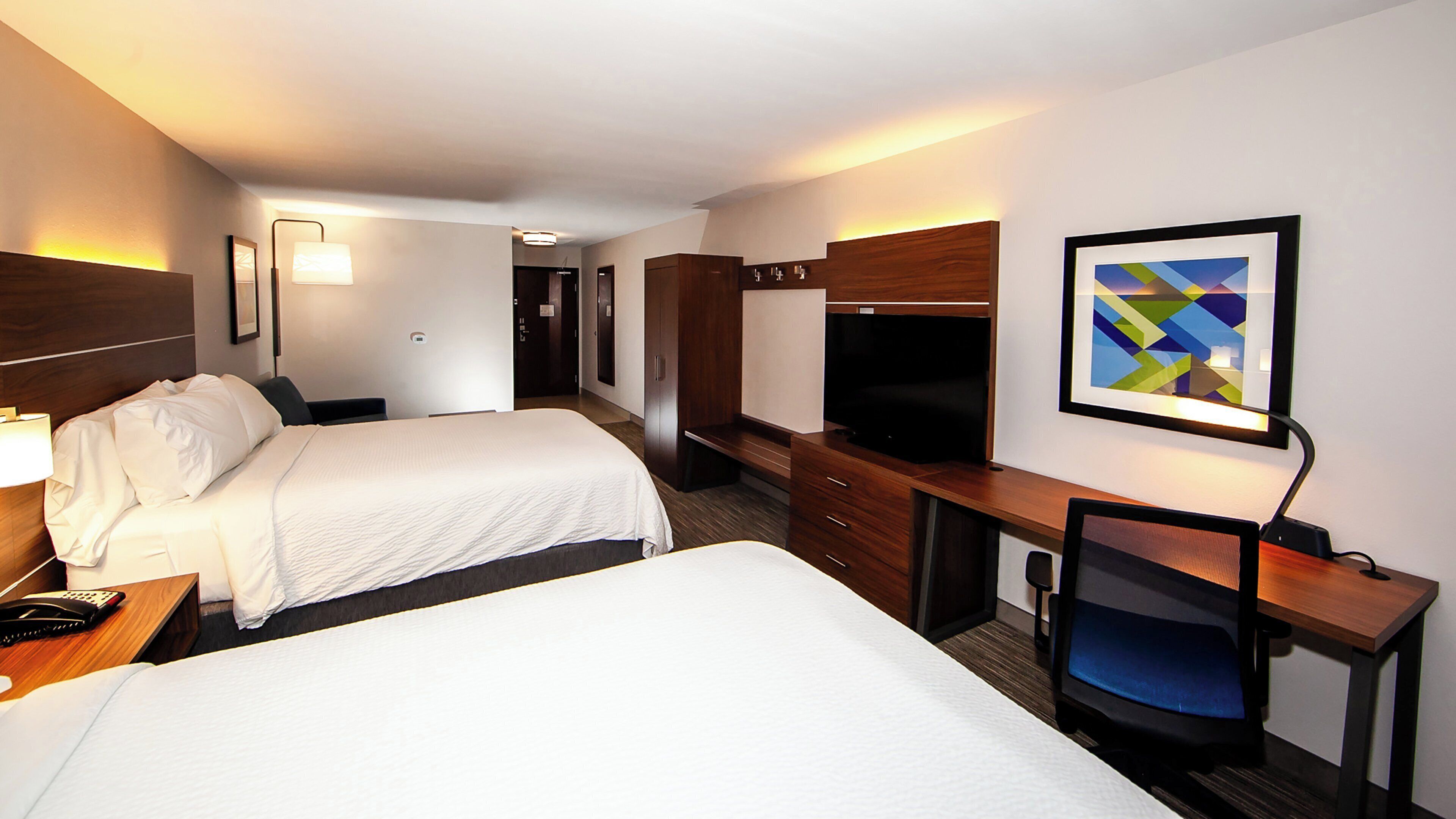 A hotel room with two beds, a desk with a chair, a television, and a framed picture on the wall.