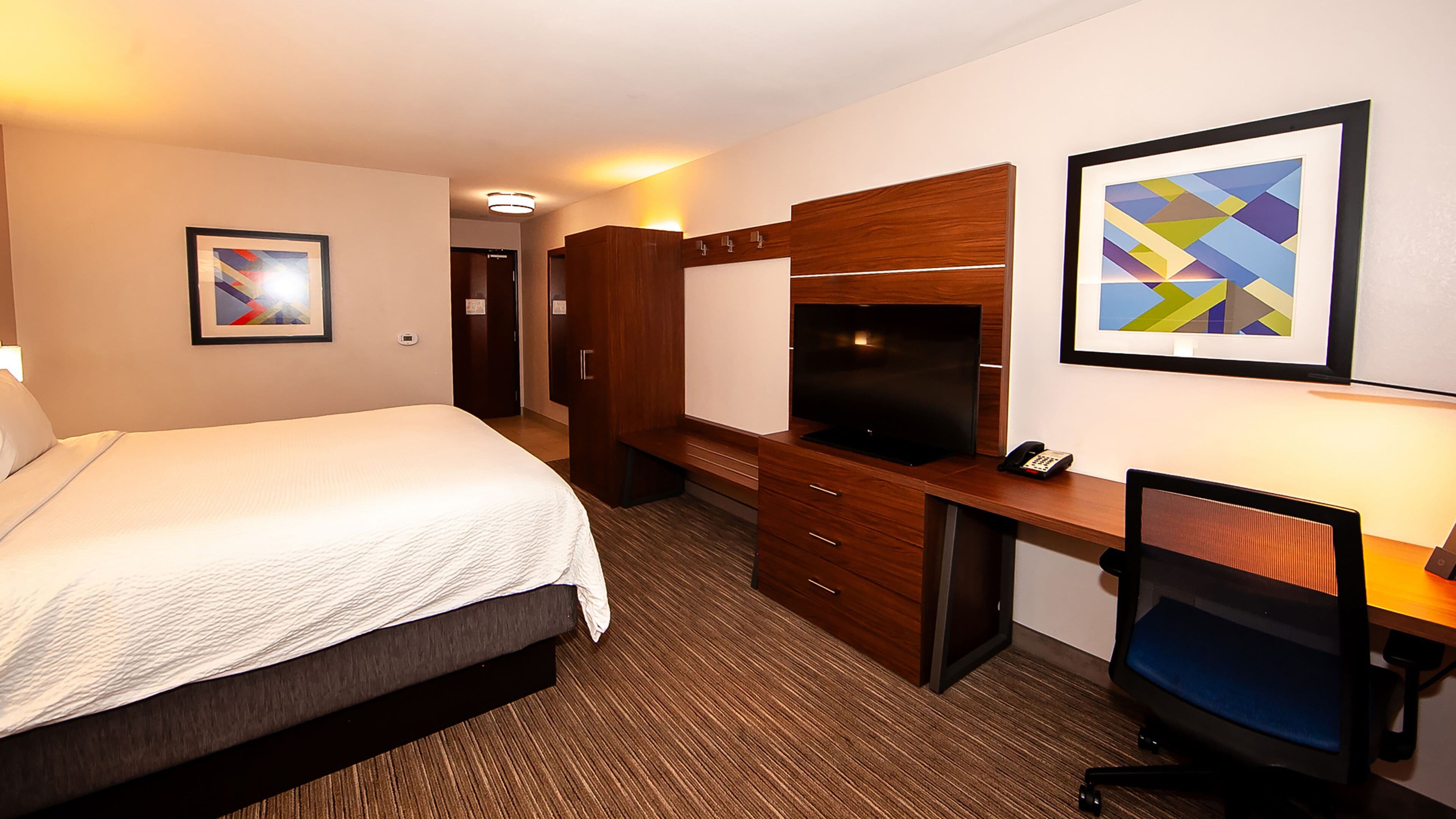 A hotel room with a bed, a desk with a computer, a TV, and a phone.