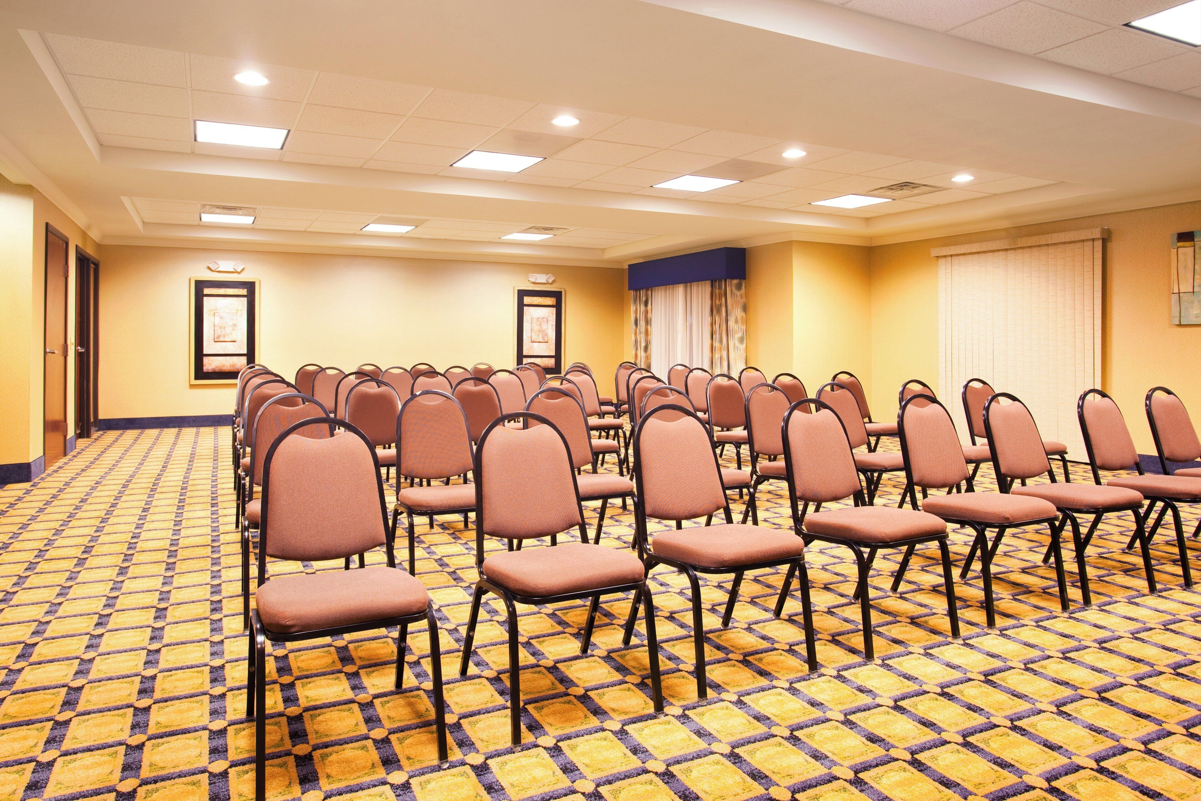Un salón de conferencias con filas de sillas, una alfombra estampada e iluminación empotrada en el techo.