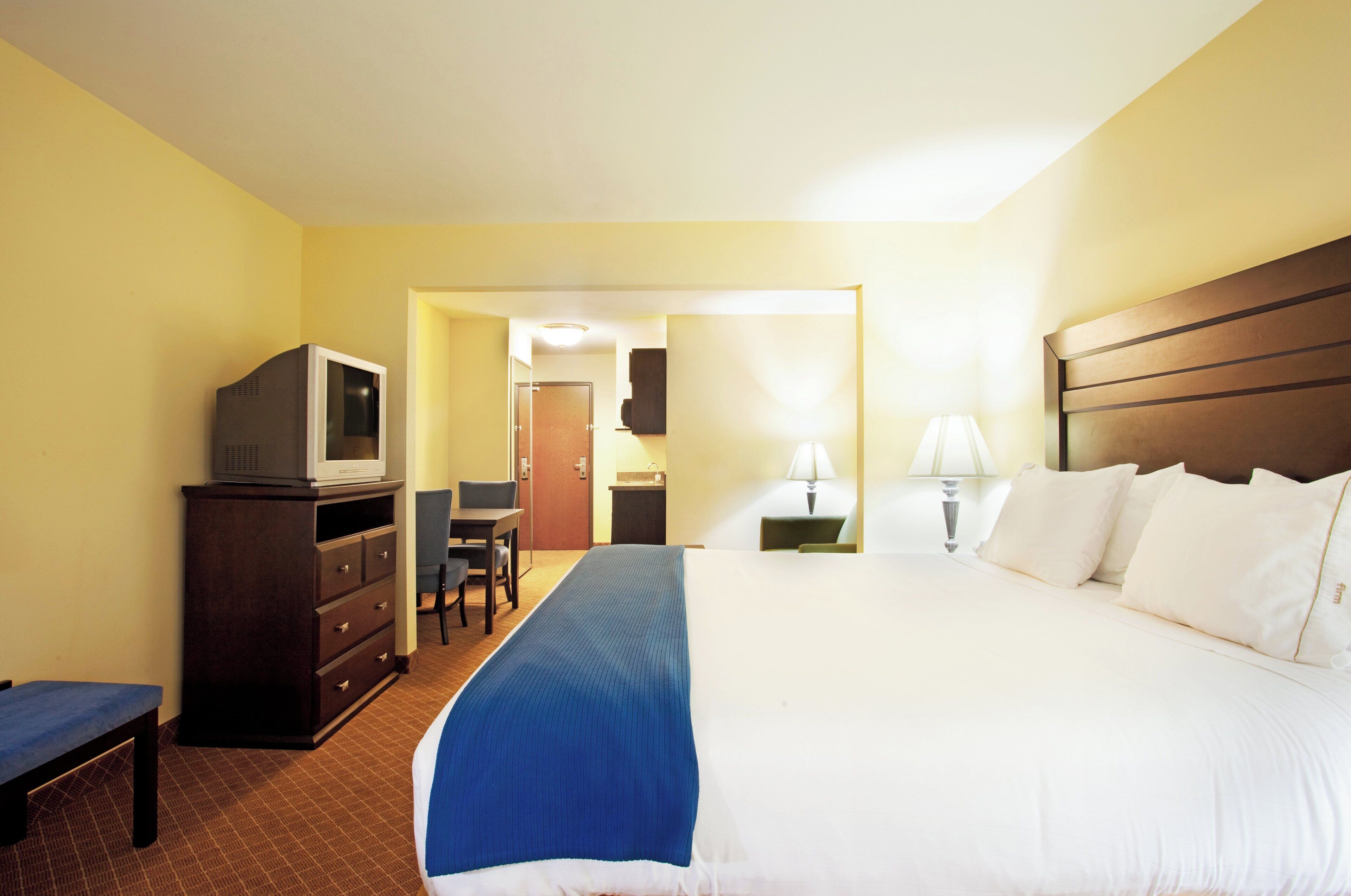 Une chambre d’hôtel avec un lit, un bureau, une chaise, un téléviseur posé sur une commode et une lampe.