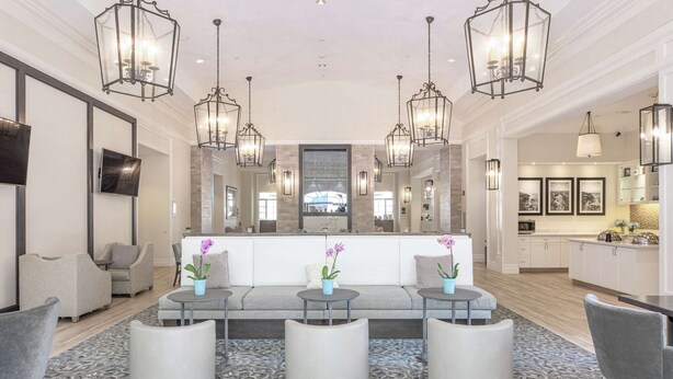 A spacious lobby with a central seating area, modern lighting fixtures, and a view into the kitchen. - Homewood Suites by Hilton Palm Beach Gardens (Palm Beach Gardens)