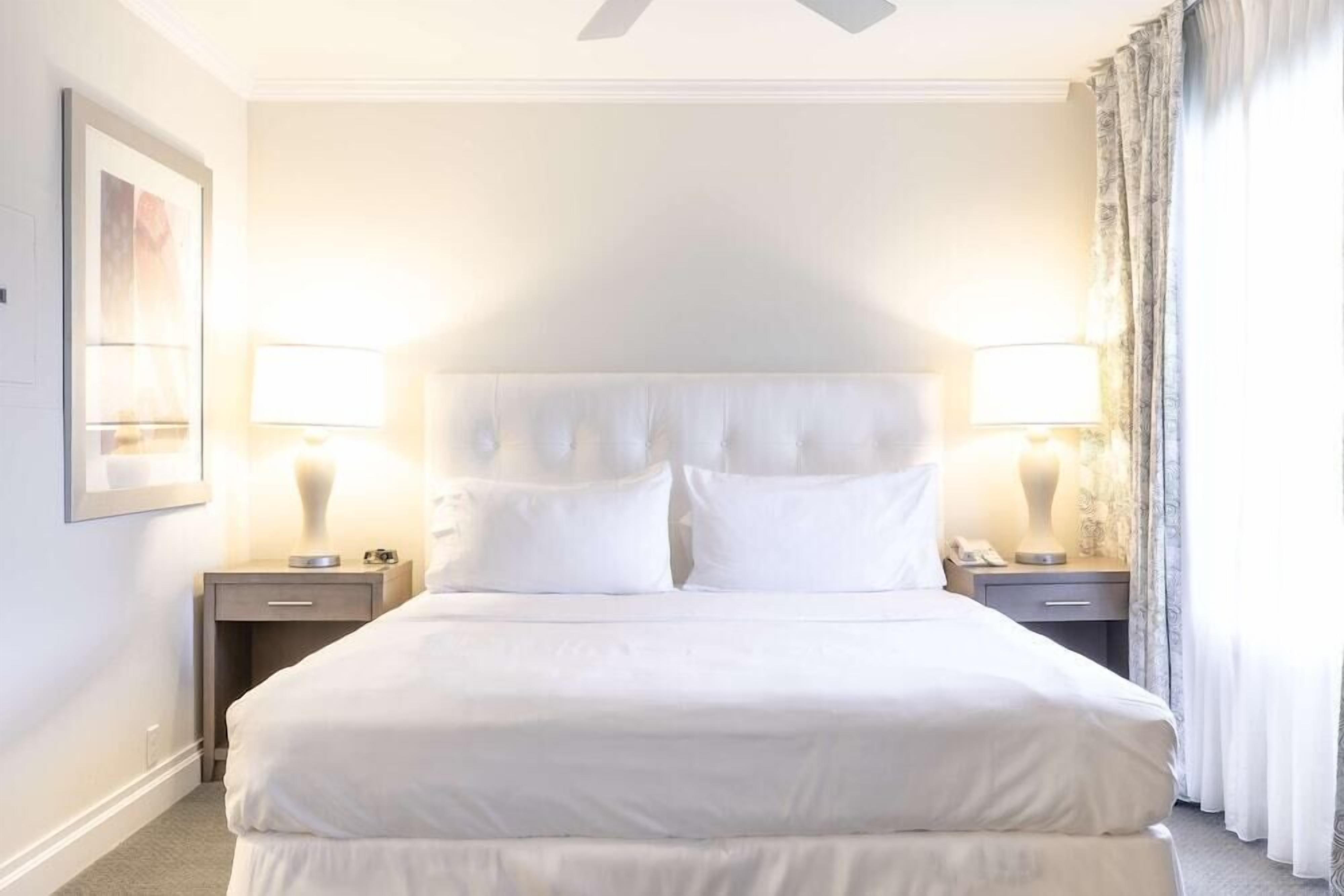 Une chambre d’hôtel avec un grand lit, deux tables de chevet, un ventilateur de plafond et une fenêtre avec des rideaux.