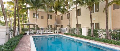 A swimming pool surrounded by palm trees and a building with multiple windows.