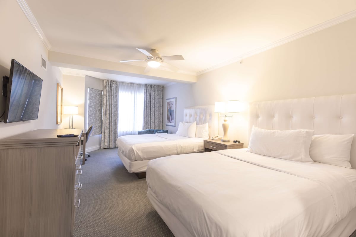 Une chambre d’hôtel avec deux lits, un bureau, une télévision et un ventilateur de plafond.