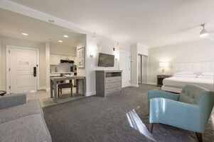 Una habitación de hotel con cama, escritorio, silla, televisor y kitchenette.