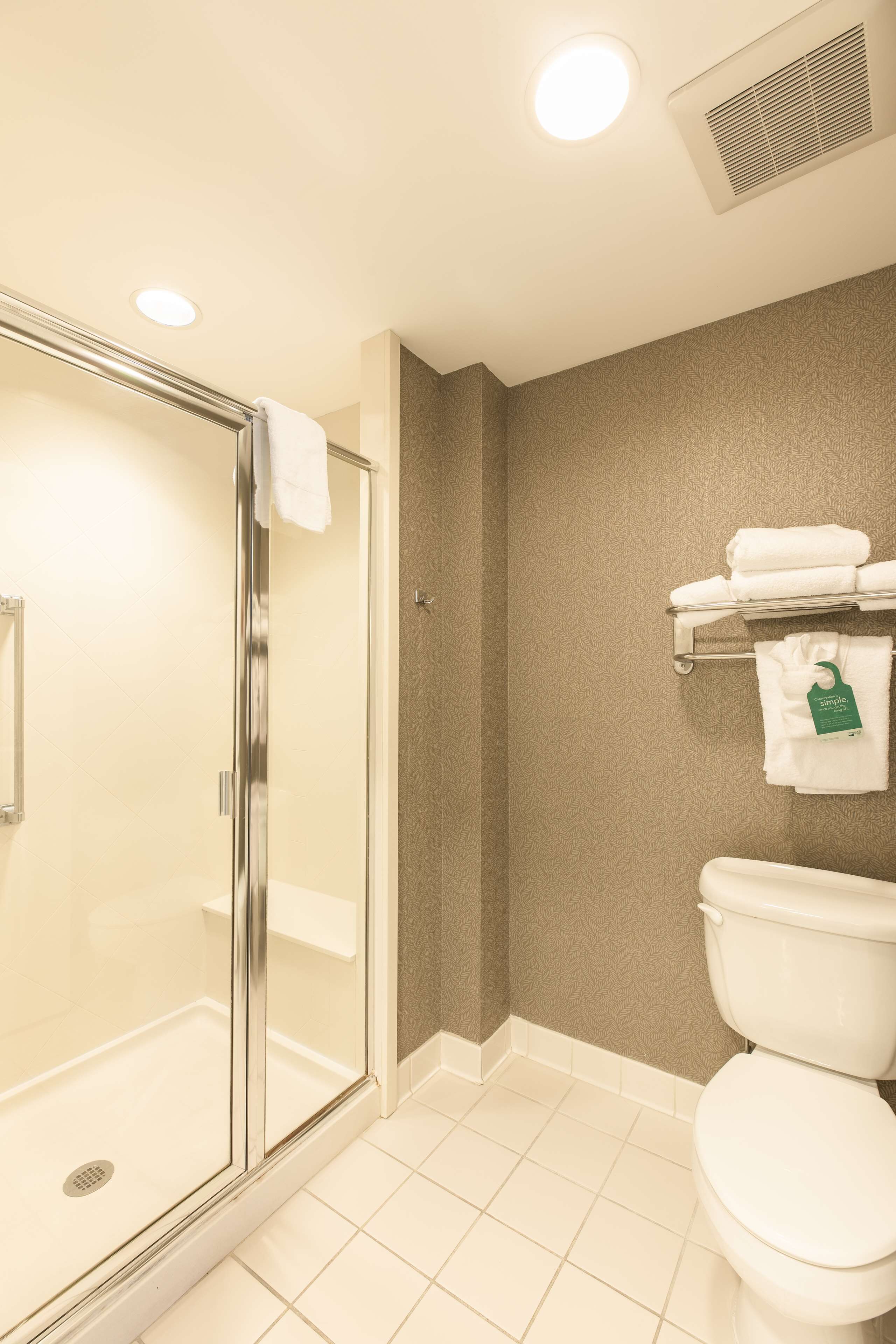 Un baño con cabina de ducha de vidrio, inodoro y toallero con toallas dobladas.