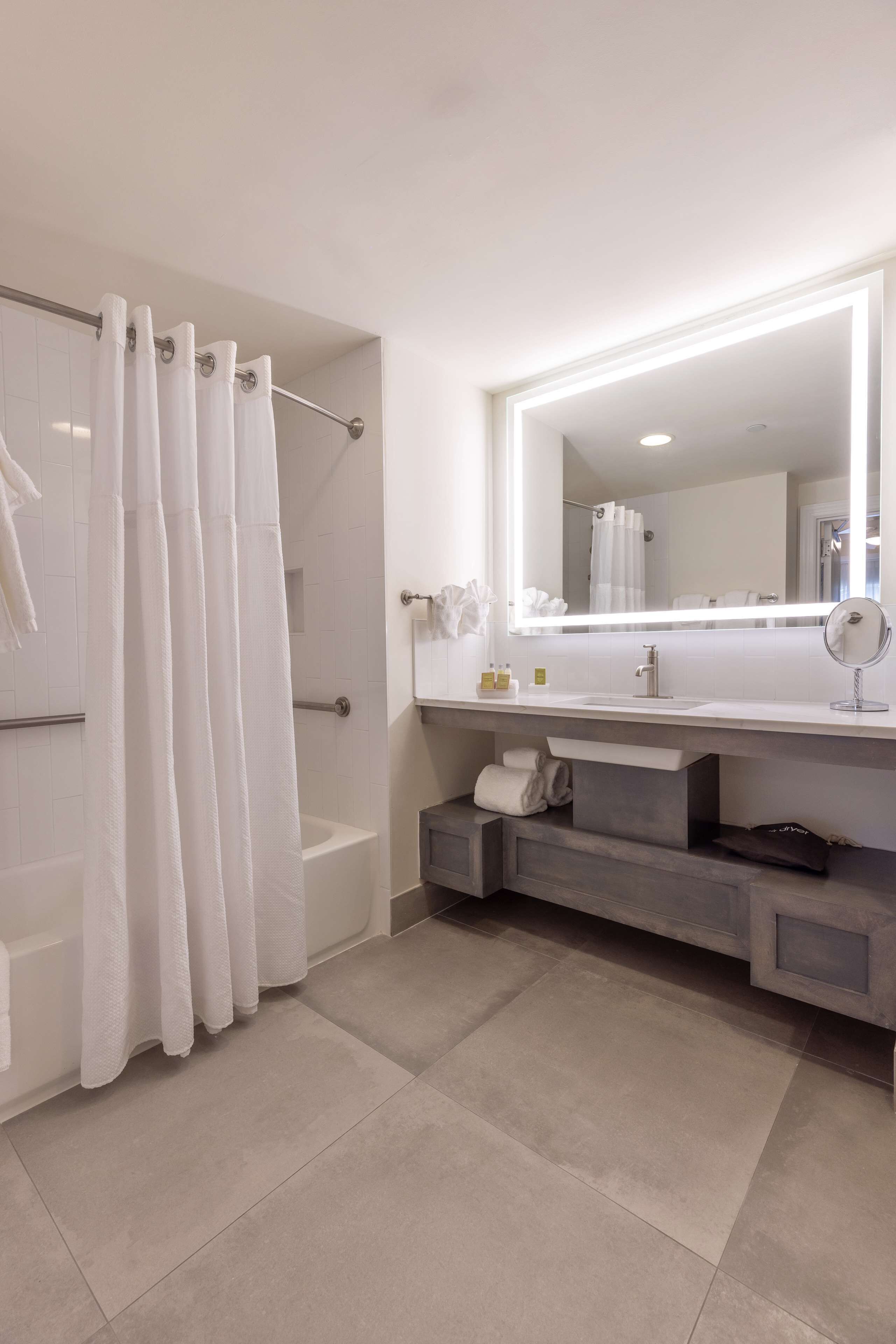 A modern bathroom with a bathtub, a large mirror, and a vanity with a sink.