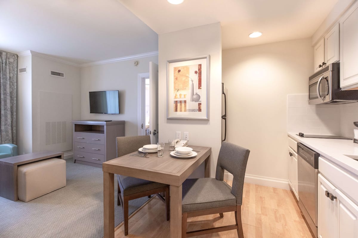 Un espace de vie compact comprenant un coin repas, une kitchenette et un téléviseur fixé au mur.
