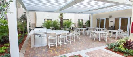 An outdoor patio area with a grill, white tables and chairs, and potted plants.
