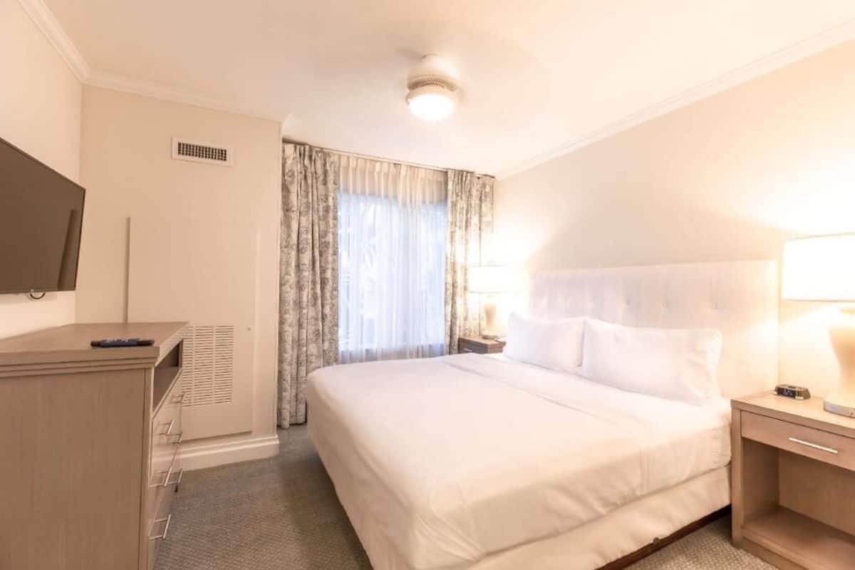 Une chambre d’hôtel comprenant un lit, une table de chevet, une lampe, une télévision et une armoire.