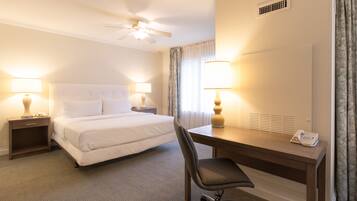 A hotel room with a bed, desk, chair, lamps, and a ceiling fan.