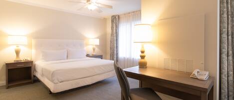 A hotel room with a bed, desk, chair, lamps, and a ceiling fan.