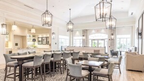 A spacious dining area with multiple tables and chairs, a patterned rug, and pendant lighting. - Homewood Suites by Hilton Palm Beach Gardens (Palm Beach Gardens)