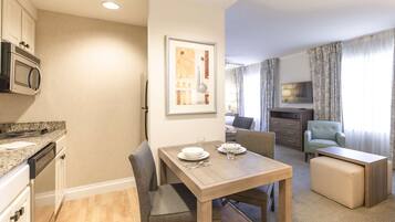 Una cocina moderna con microondas integrado, un comedor con mesa de madera y sillas grises tapizadas, y una sala de estar con sofá y televisor.