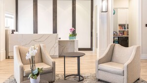 A modern hotel lobby with two armchairs, a marble reception desk, and a small table with a vase of flowers. - Homewood Suites by Hilton Palm Beach Gardens (Palm Beach Gardens)