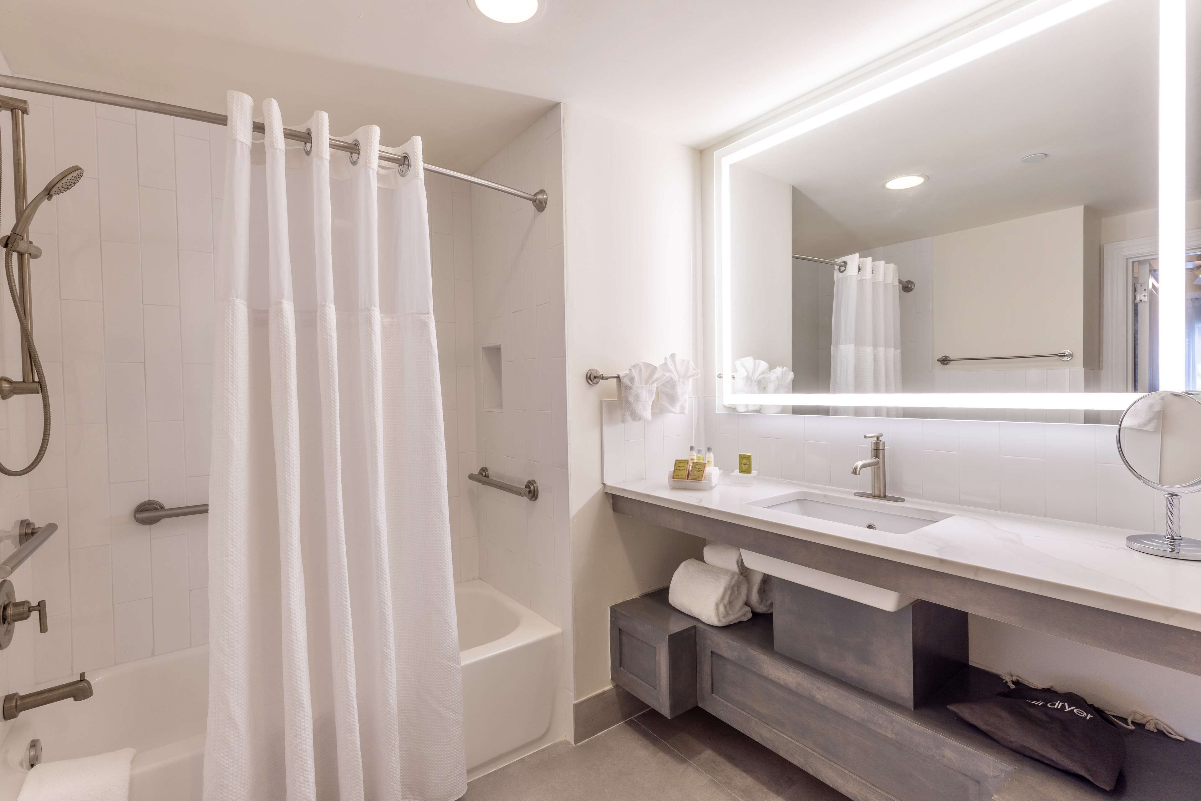 A modern bathroom with a bathtub, shower, and a large mirror above the sink.