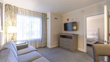 A hotel room with a sofa, a television, a bed, and a chair.