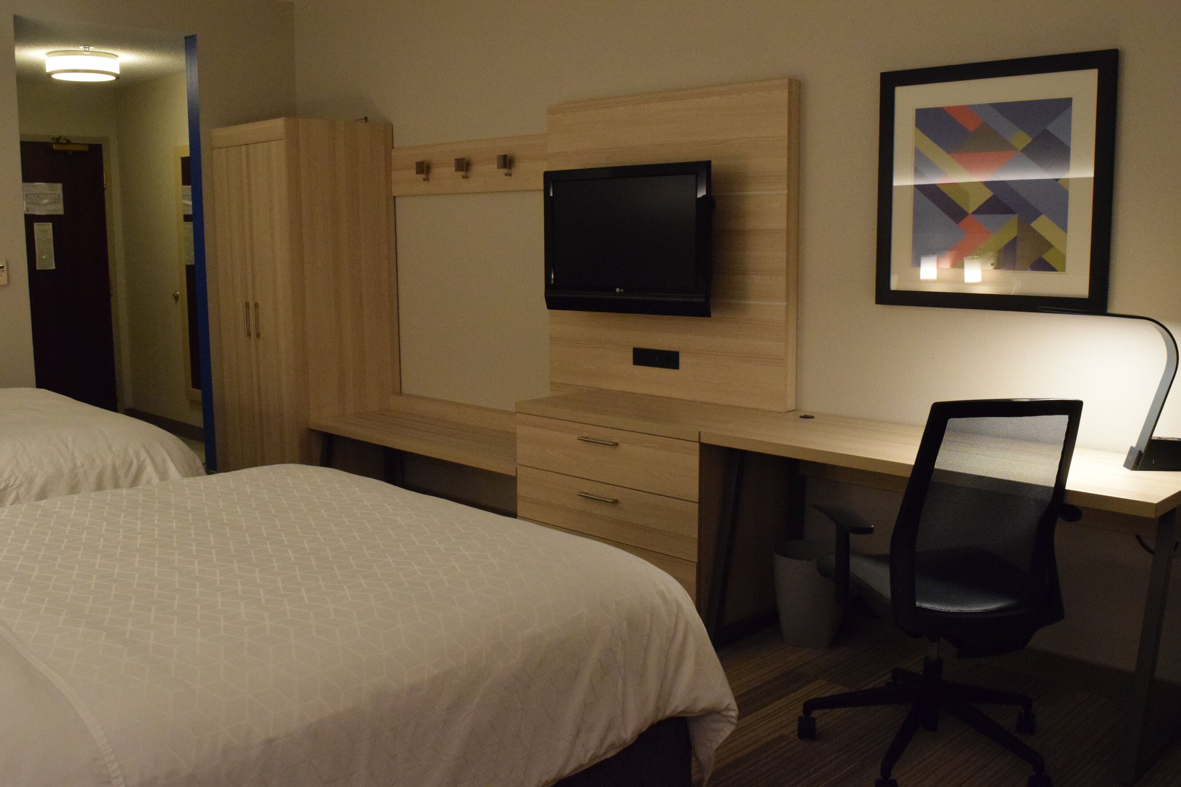A hotel room with two beds, a desk with a computer, a TV, and a framed picture on the wall.