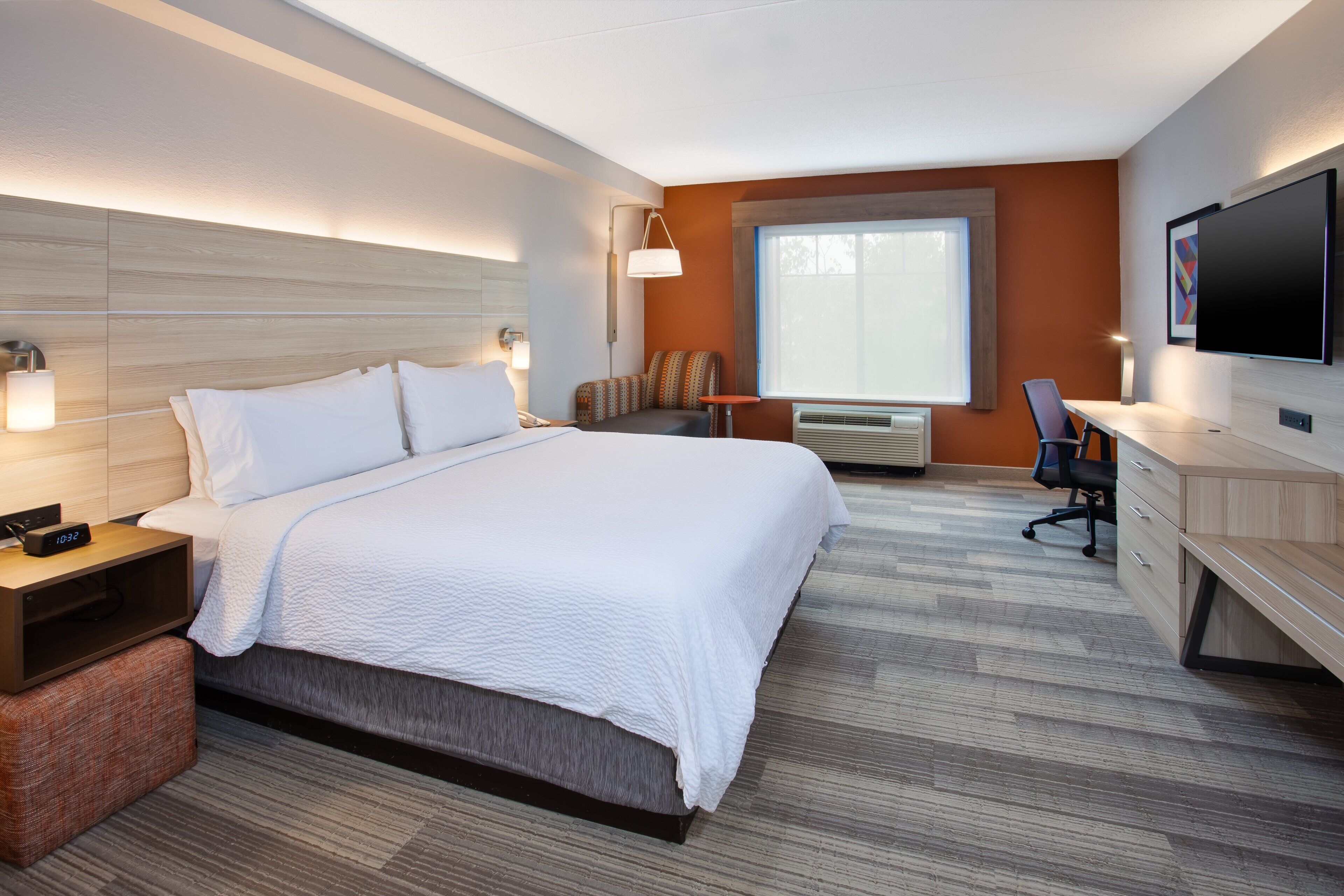 A modern hotel room with a large bed, a desk, a chair, a flat-screen TV, and a window with blinds.