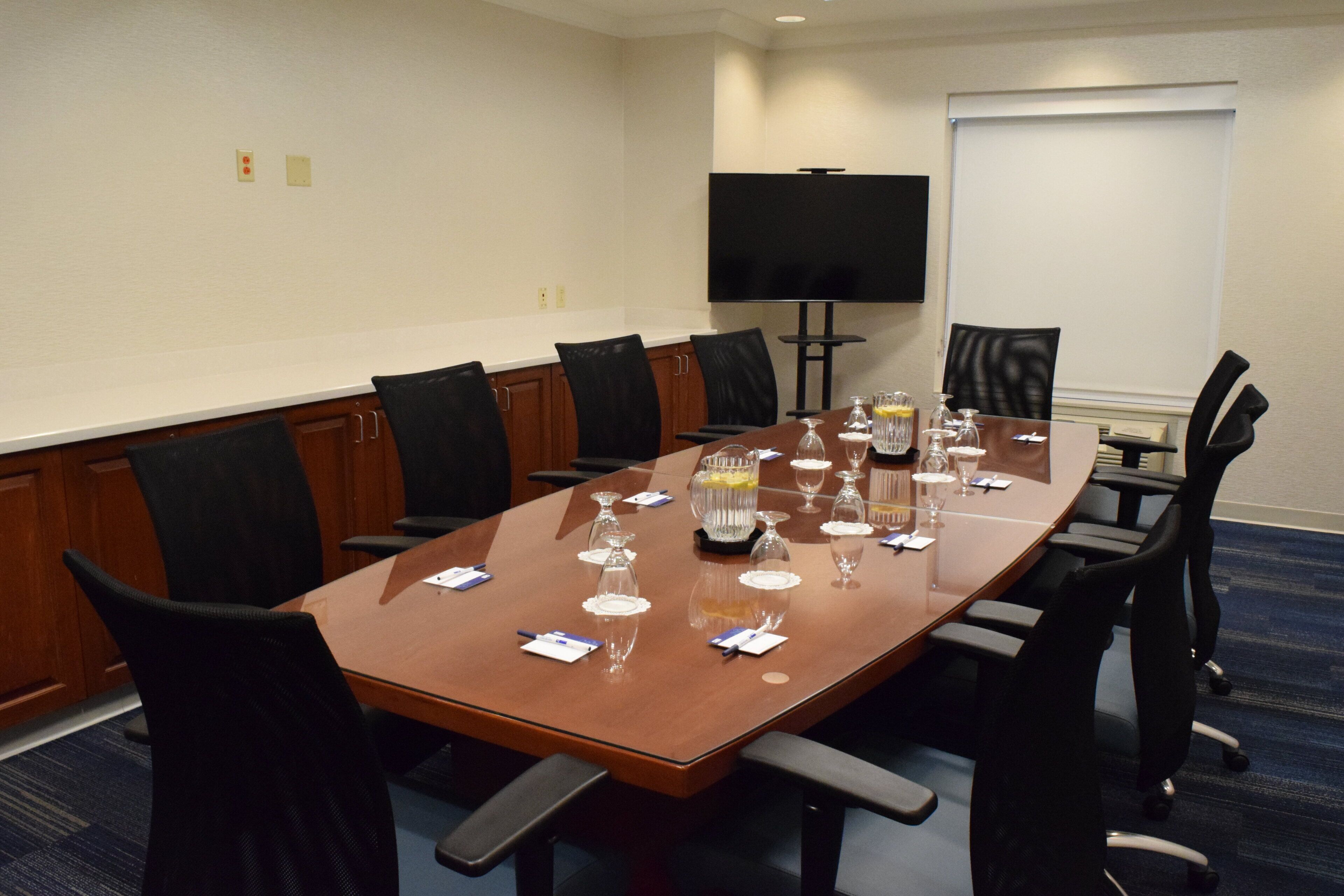 A conference room with a long table, chairs, a TV, and a whiteboard.