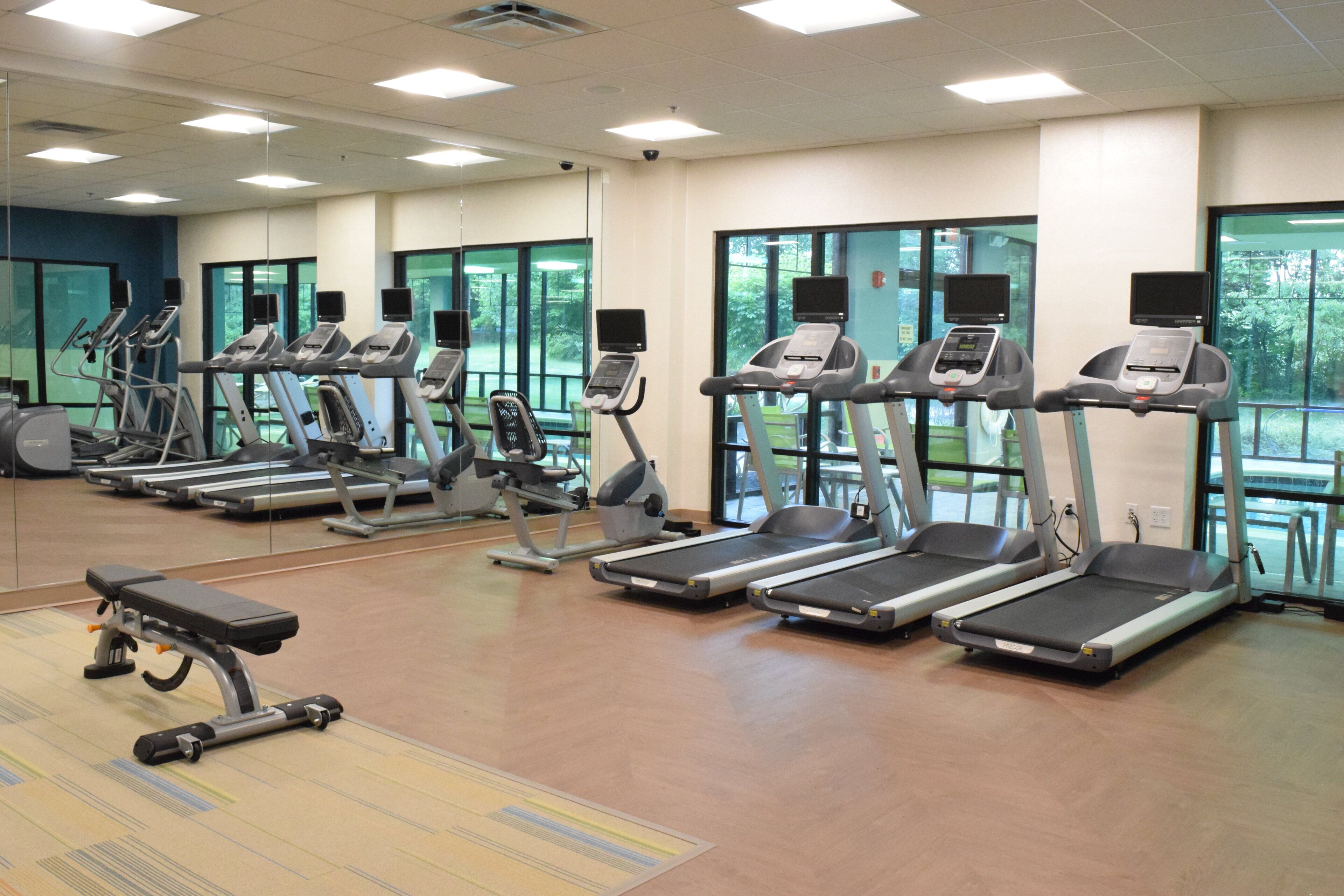 Un gimnasio con cintas de correr, bicicletas estáticas y una banca.