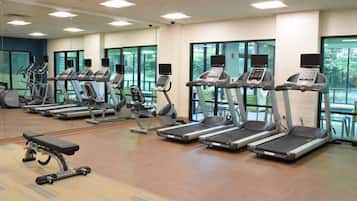 Un gimnasio con cintas de correr, bicicletas estáticas y una banca.