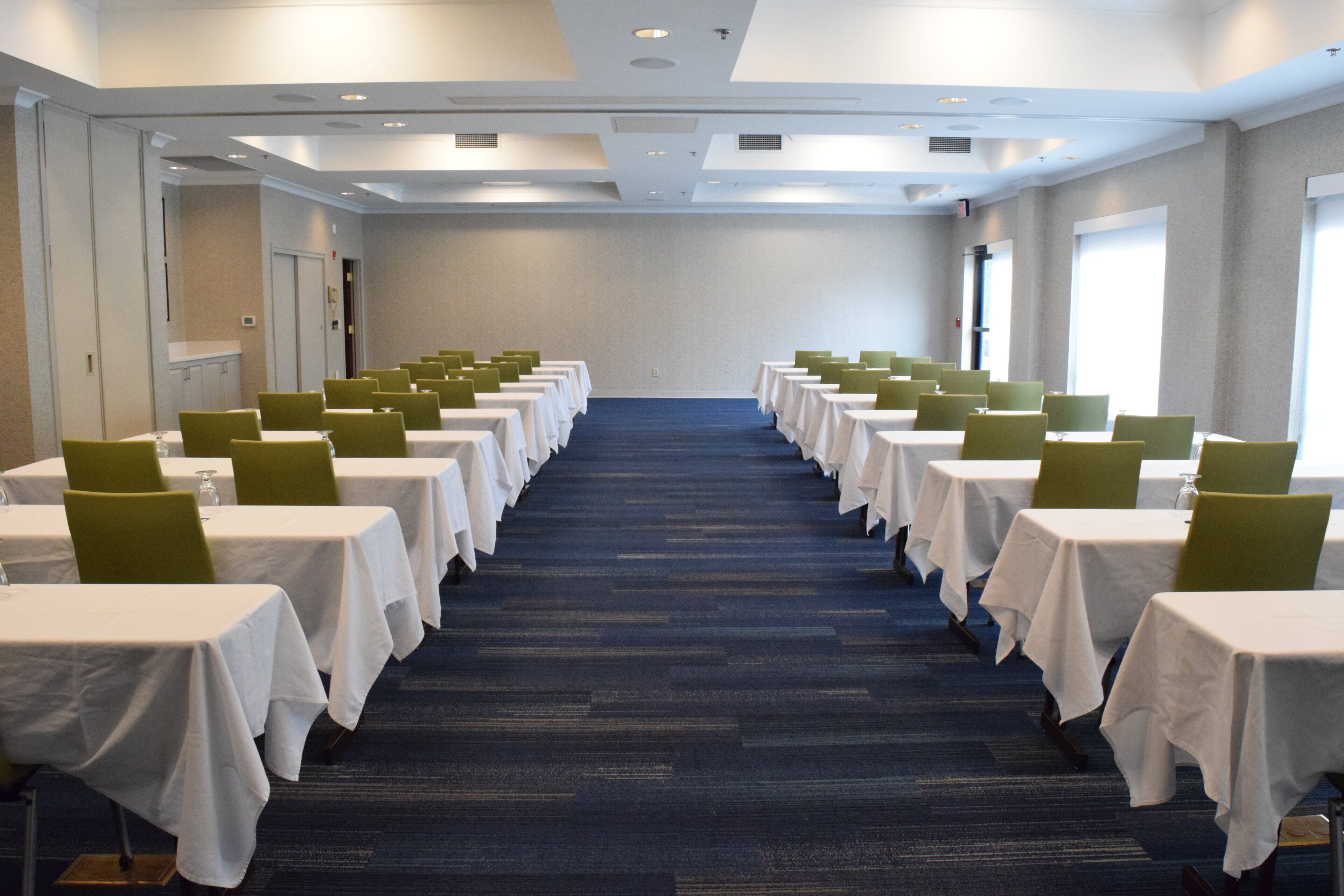 Un salón de conferencias con filas de mesas y sillas, piso alfombrado y una decoración en tonos neutros.