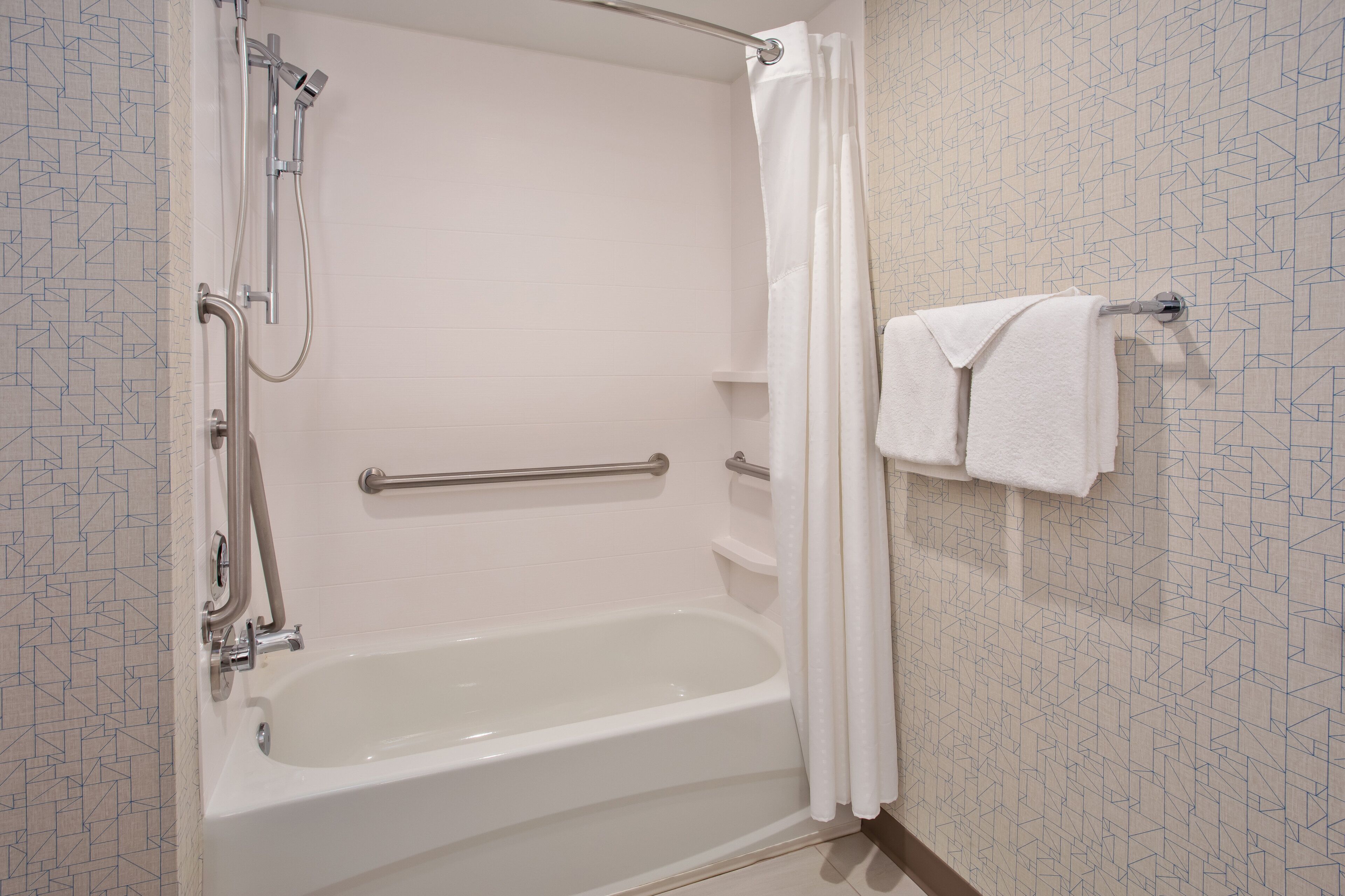 A bathroom with a bathtub, shower, and handrails.