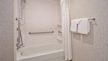 A bathroom with a bathtub, shower, and handrails.