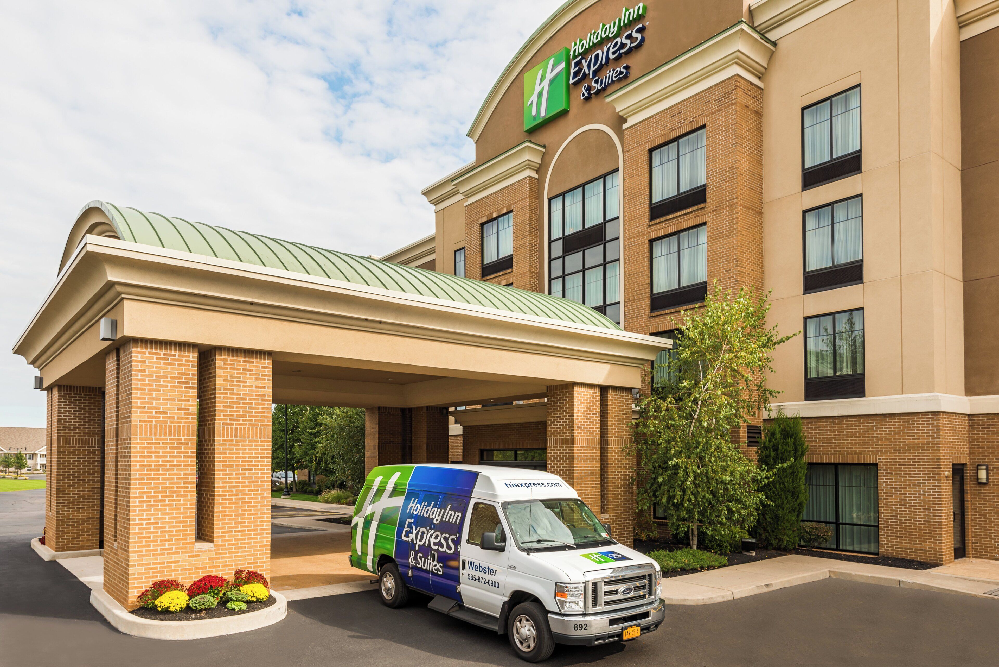 A Holiday Inn Express & Suites building with a covered entrance and a service van parked in front.