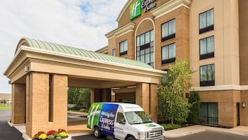 A Holiday Inn Express & Suites building with a covered entrance and a service van parked in front.