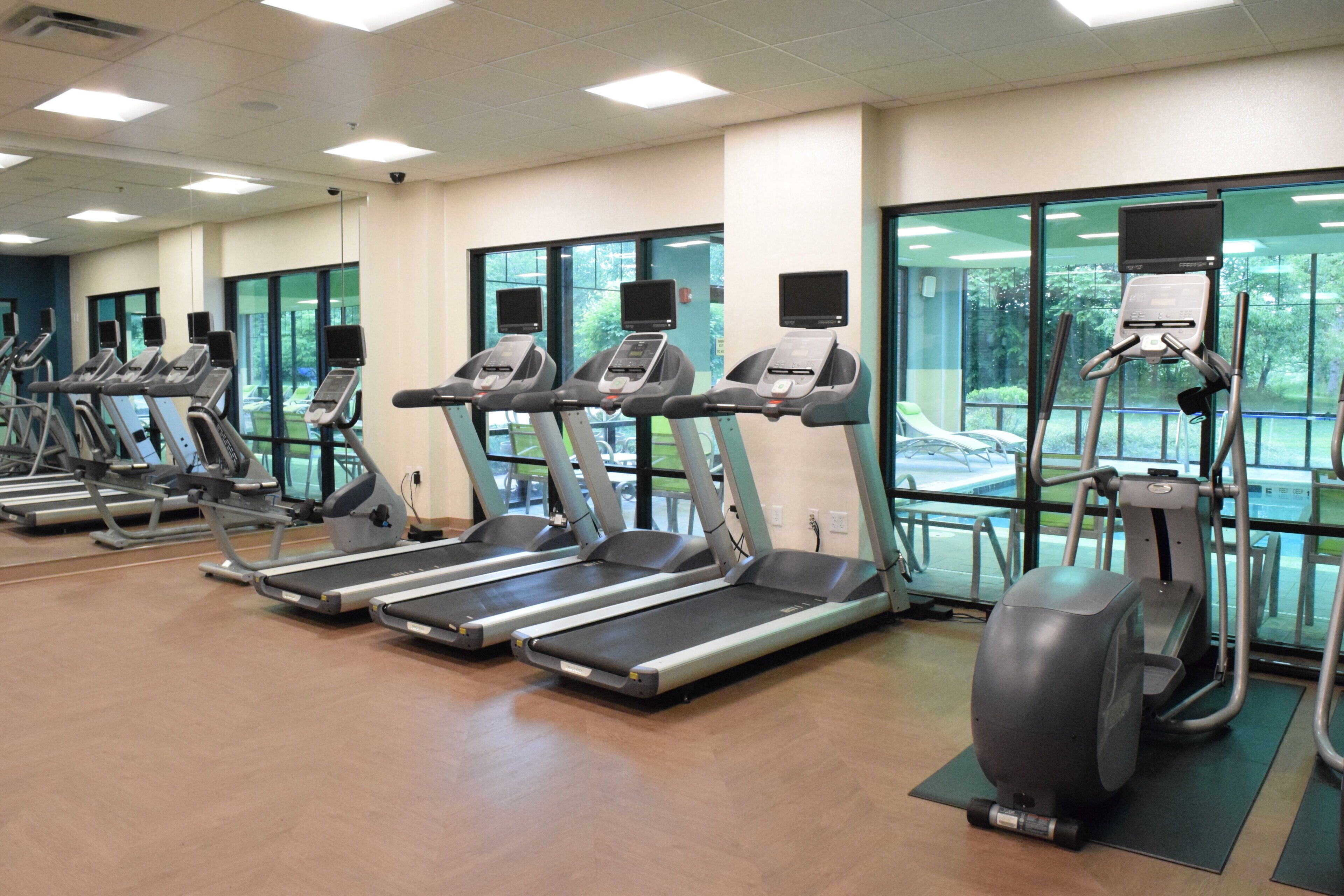 A gym with multiple treadmills and exercise bikes, large windows, and a view of the outdoors.